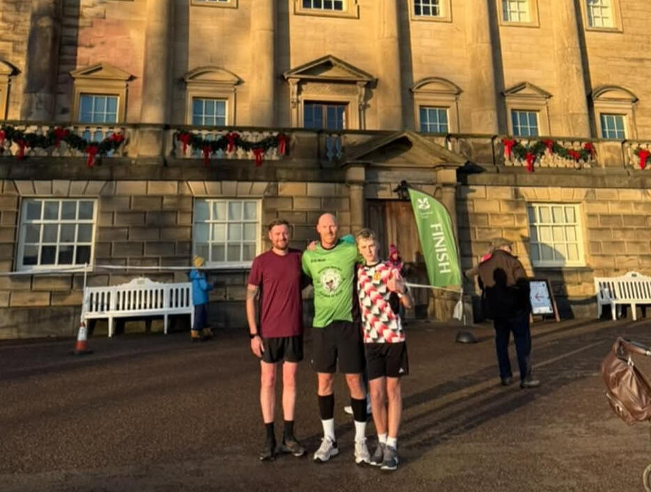 Group photo of man with club shirt standing two other runners, backdrop of old mansion.