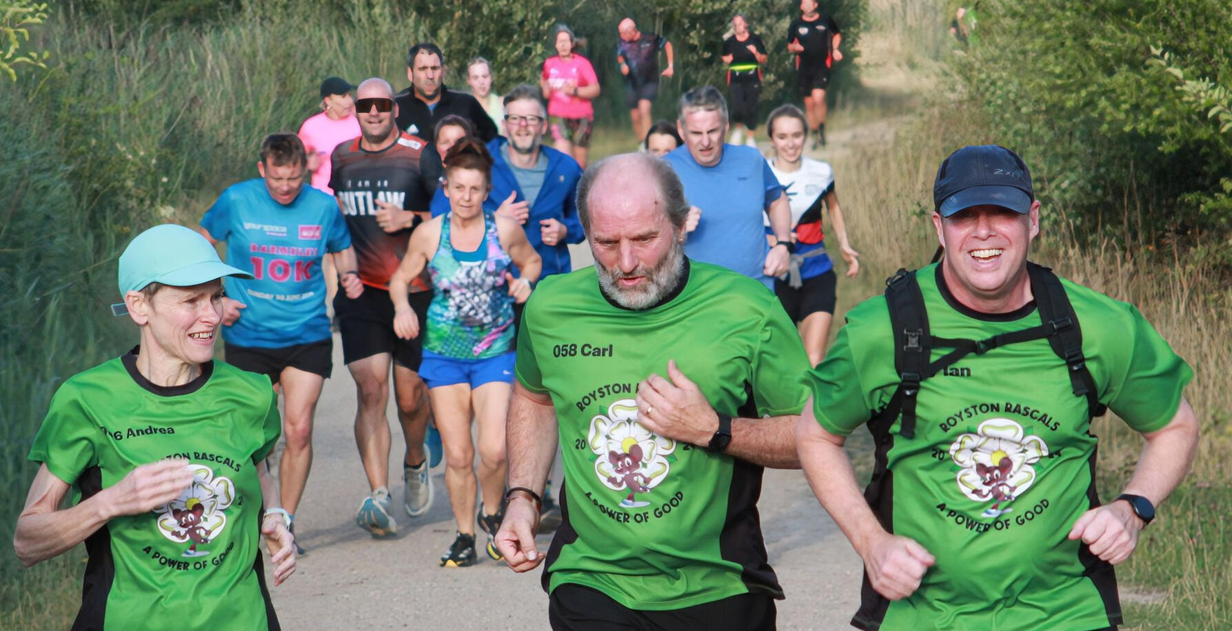 Action shot of three people in club shirts running towards camera on gravel path.